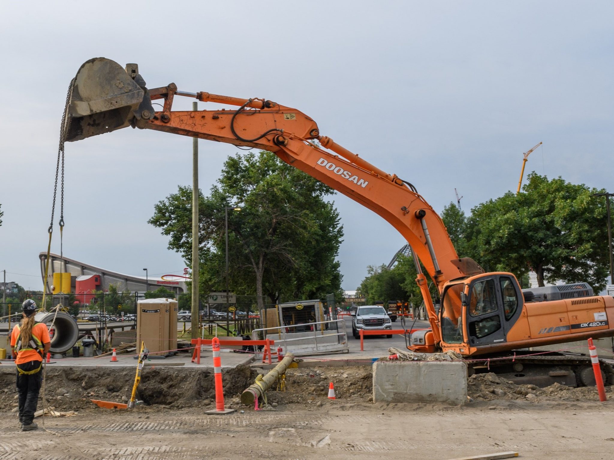 Excavator lifting and moving a pipe into place as a construction worker watches in Beltline East on 12 Avenue S.E.