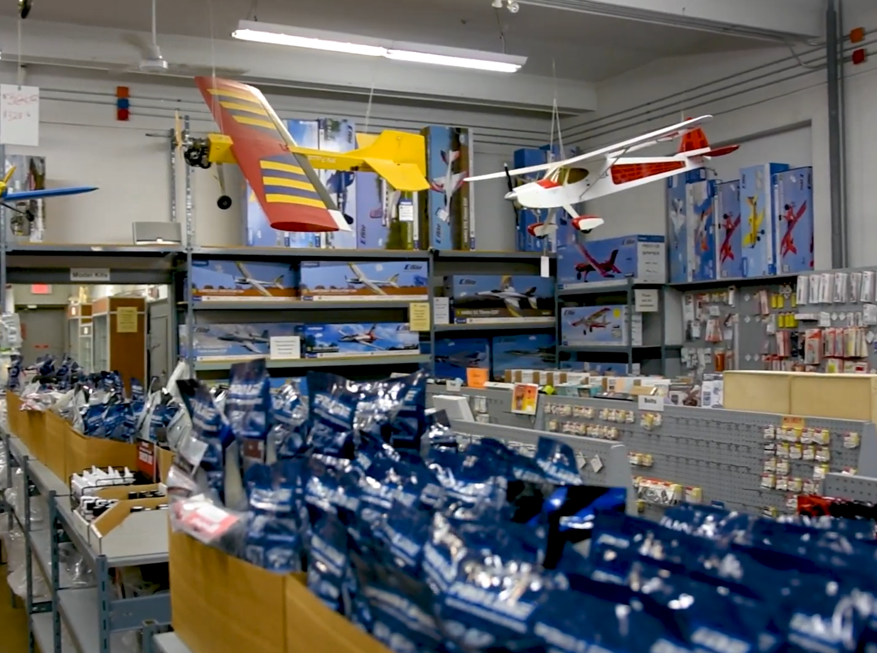 Interior of Action Hobby showing shelving with products and model planes suspended from the ceiling