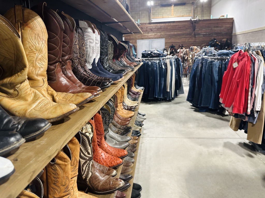 Selection of cowboy boots on shelves and racks of clothing at Rein It In.