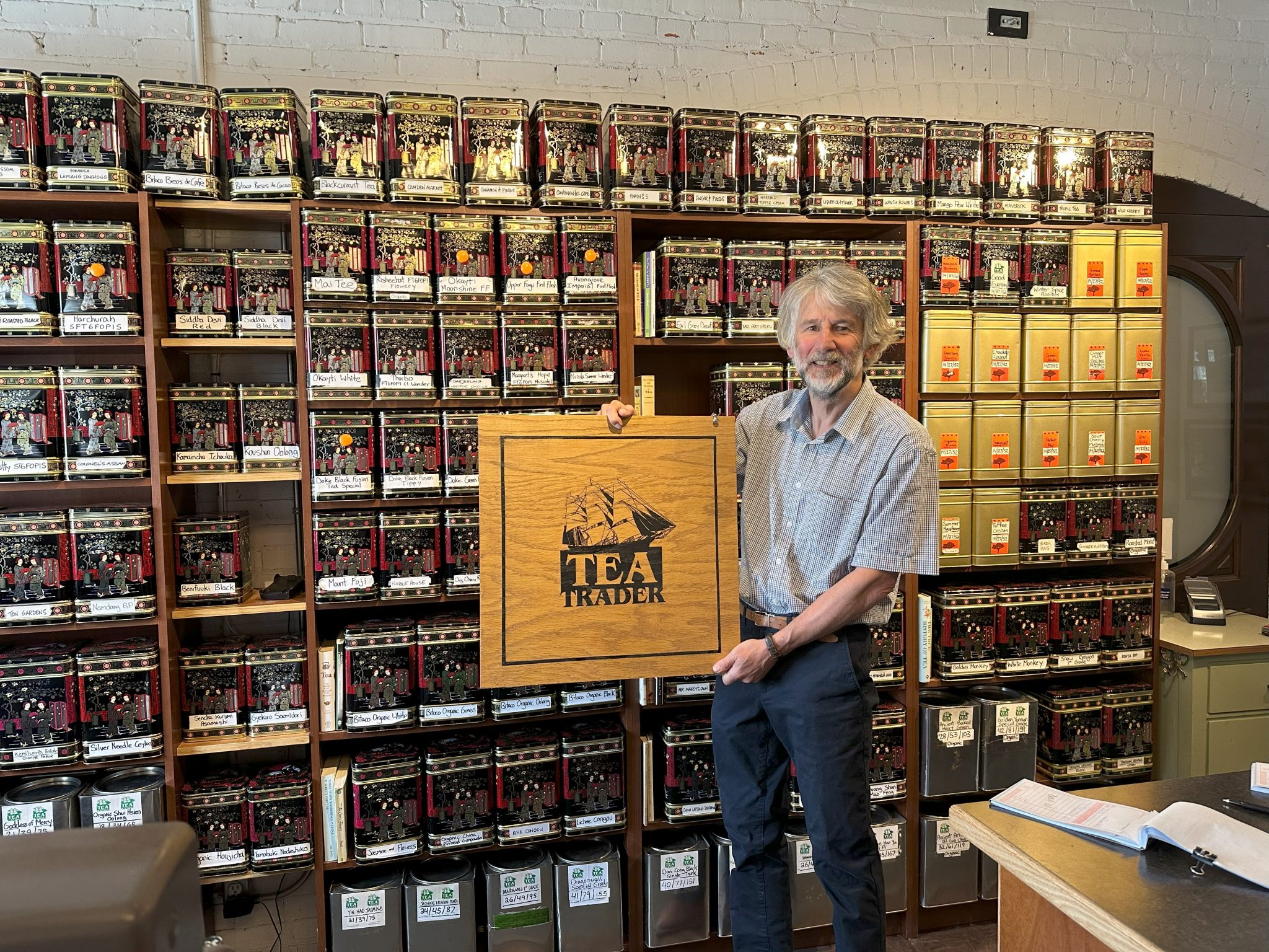 Ted Jones standing in front of a wall of tea, holding a Tea Trader sign.