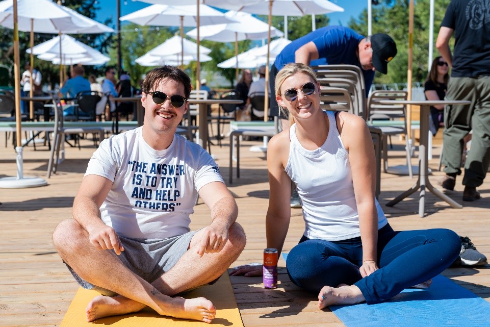 A man and woman sitting on yoga mats outside in the summer